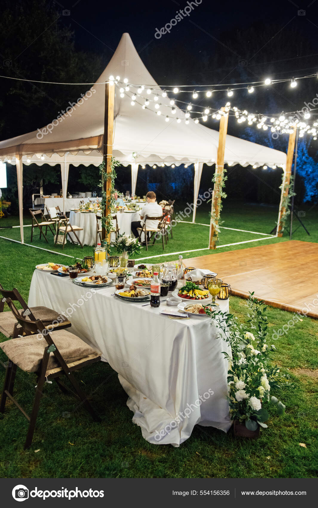 Wedding. Banquet. The chairs and round table for guests, served with cutlery, greenery flowers and crockery and covered with a white tablecloth. olive color. Evening time